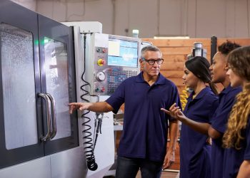 An instructor explains CNC machine operation to a group of students in a manufacturing training environment