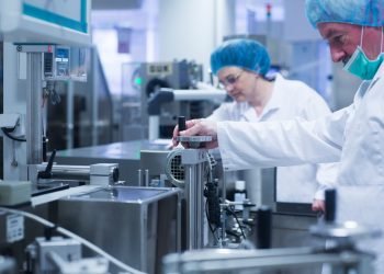 Pharmaceutical workers in cleanroom attire adjusting equipment on a production line