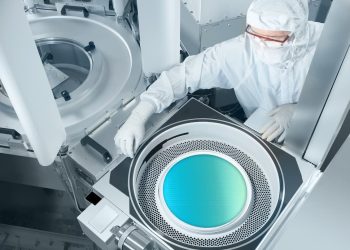 Engineer in cleanroom attire working at an open semiconductor process chamber with a silicon wafer inside