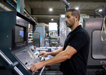 Machinist operating the control panel of a CNC machine tool on a machine shop floor