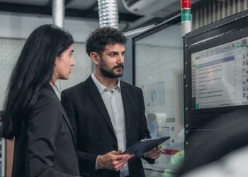 Two business professionals reviewing production data on a control panel screen in a manufacturing plant