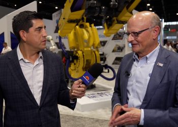 Danny Gonzales interviews Acme Manufacturing President and CEO Fritz Carlson in front of a yellow FANUC robotic arm at the Acme booth during IMTS 2026