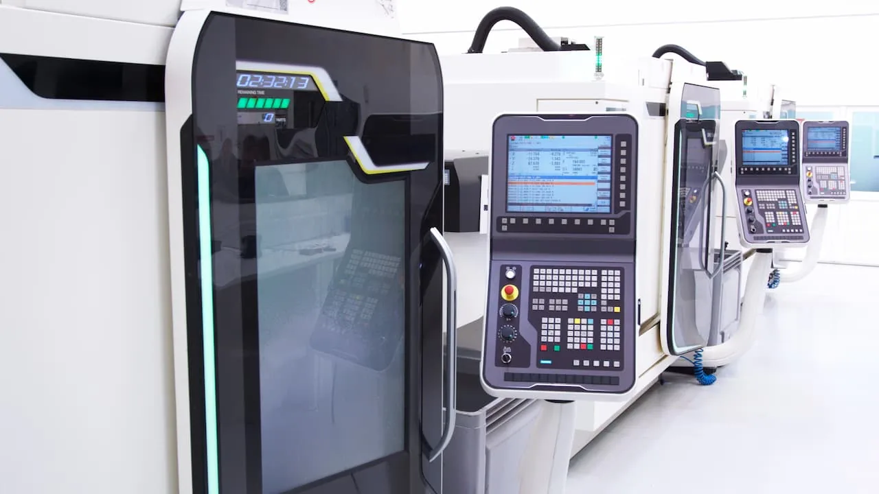 A row of enclosed CNC machining centers with control pendants in a bright machine shop