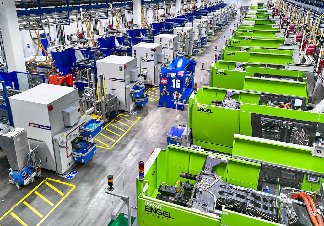 Rows of green injection moulding machines with a blue automated guided vehicle in the centre aisle of a LEGO factory