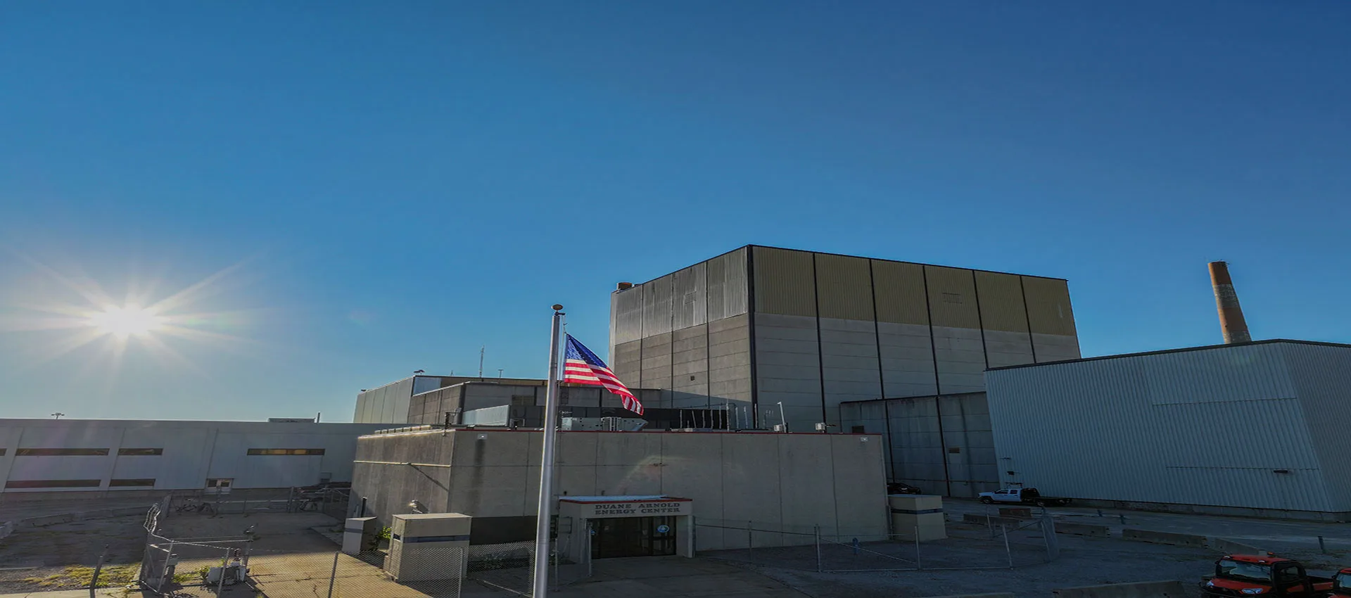 Duane Arnold Energy Center in Linn County, Iowa, its reactor building and stack lit by low sun with a US flag in the foreground